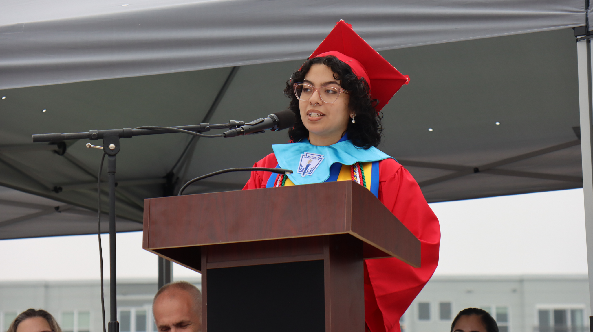 Salutatorian Angelina Agostini in a red Graduation cap and gown speaking at a podium